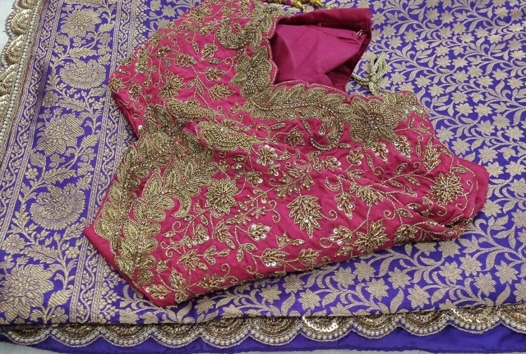 Pink blouse with maggam work embroidery on it and a saree which has embroidered scallop border kept on the table